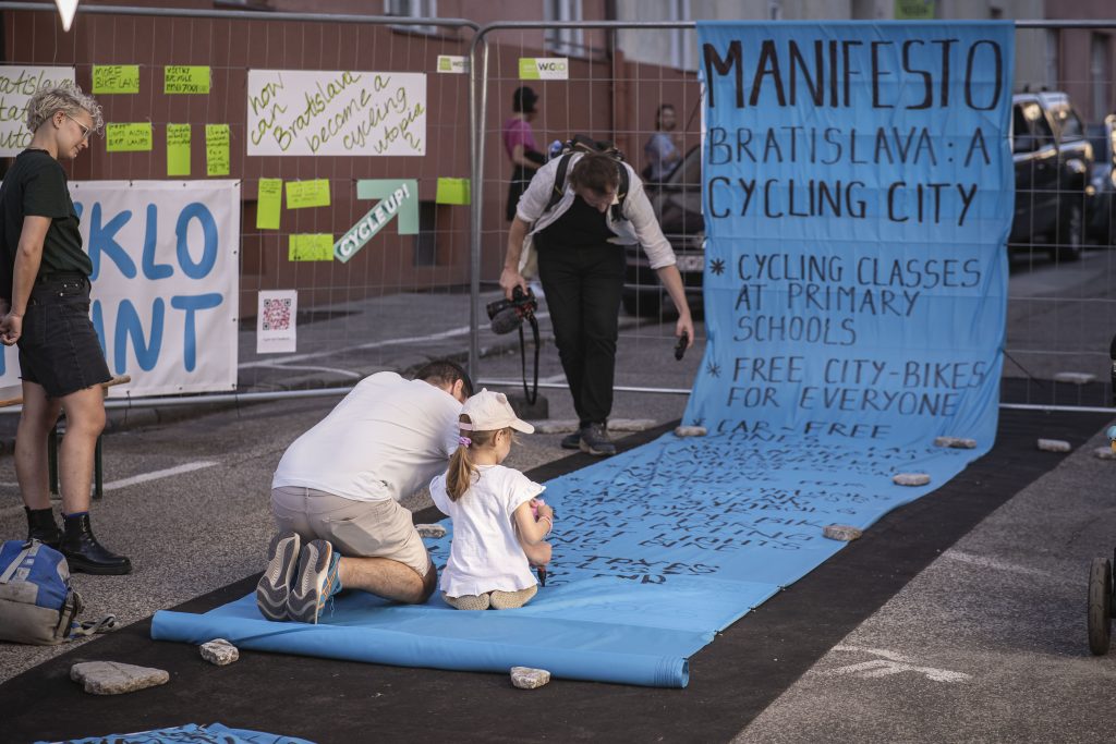an adult and a child sit on a blue fabric that has a large manifesto written on it
